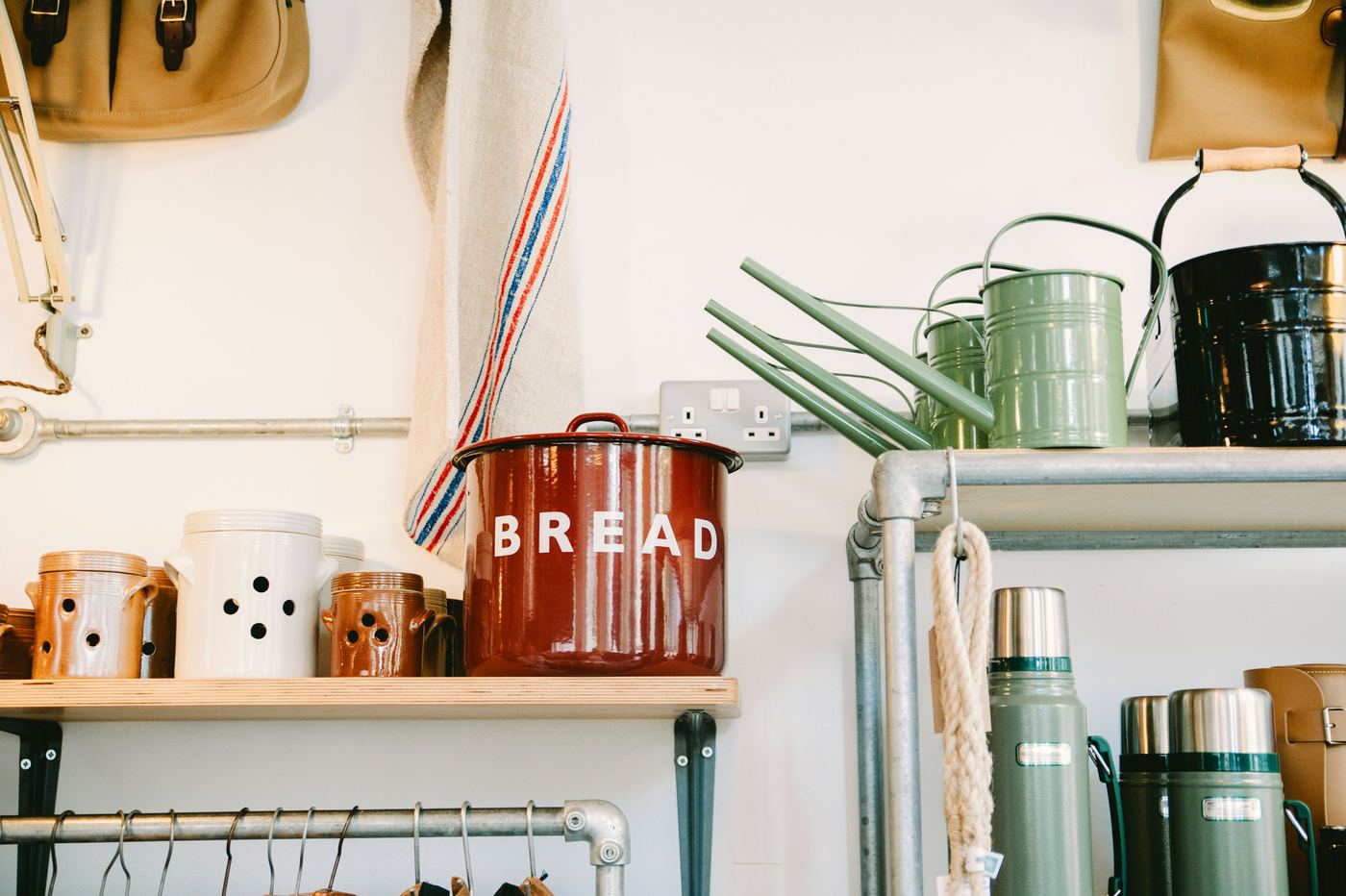Household goods including a bread bin, watering cans, and flasks on a shelf